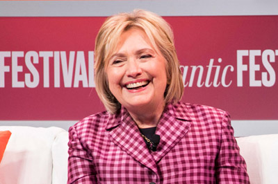 Hillary Clinton smiling in a chair with the Atlantic Festival logo behind her