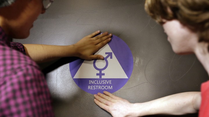 Two students place a new sticker on the door at the ceremonial opening of a gender neutral bathroom at Nathan Hale High School on May 17 in Seattle.