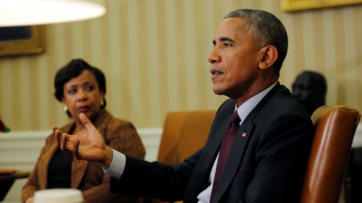 Image shows President Obama seated in a brown leather chair, right hand raised slightly, addressing someone out of the frame. Attorney General Loretta Lynch sits to his right, looking at hiim.