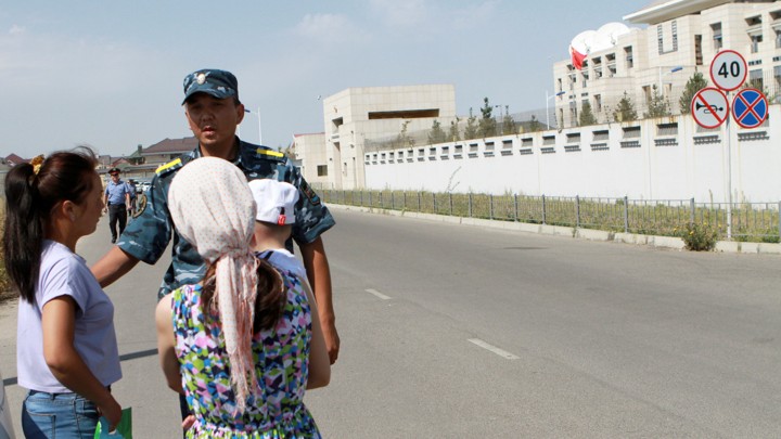 A member of Kyrgyz security forces addresses passers-by near the site of a bomb blast outside China's embassy in Bishkek, Kyrgyzstan.
