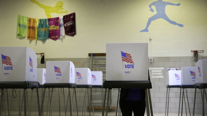 A woman stands at one of many polling booths inside an elementary-school gymnasium.
