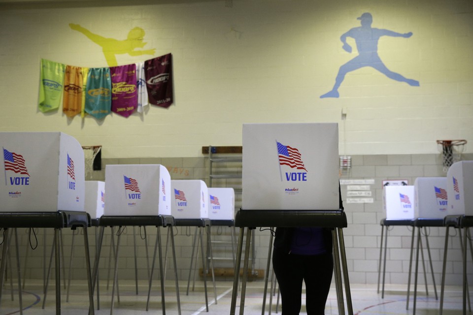 A woman stands at one of many polling booths inside an elementary-school gymnasium.