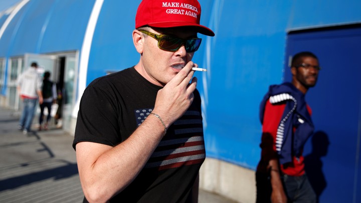 A man in a "Make America Great Again" cap smokes a cigarette.