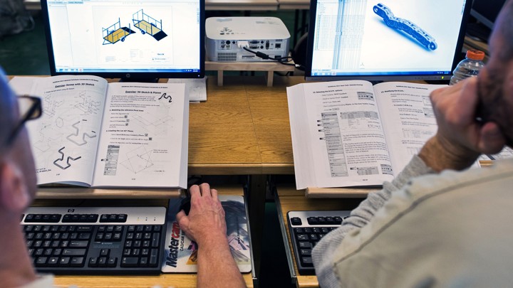Two students look at technical drawings on computers.
