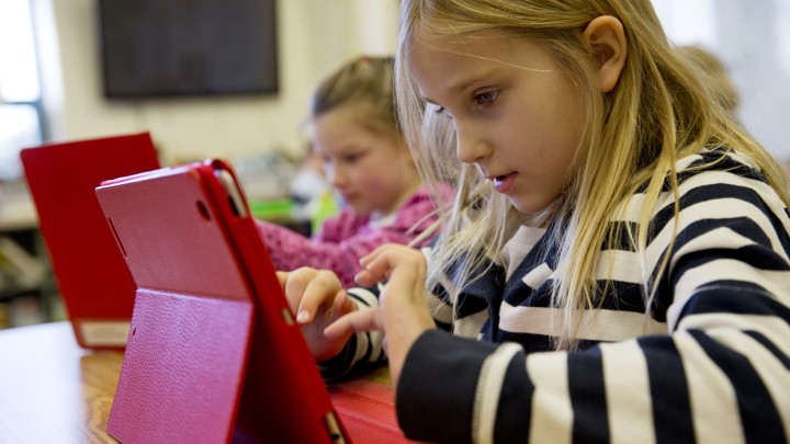 Two young girls sit at a desk with iPads.