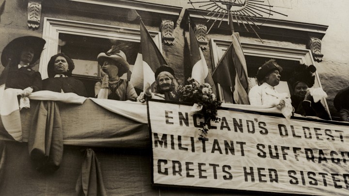 Elizabeth Wolstenholme Elmy by a banner that reads "England's Oldest Militant Suffragist Greets Her Sisters"