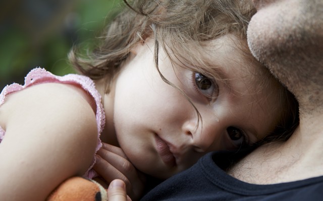 A tear streaks across sad child's nose as she rests her head on a man's chest.