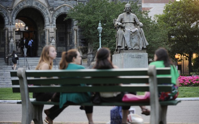 Students sit on a bench in front of a statute of the university founder John Carroll at Georgetown University.