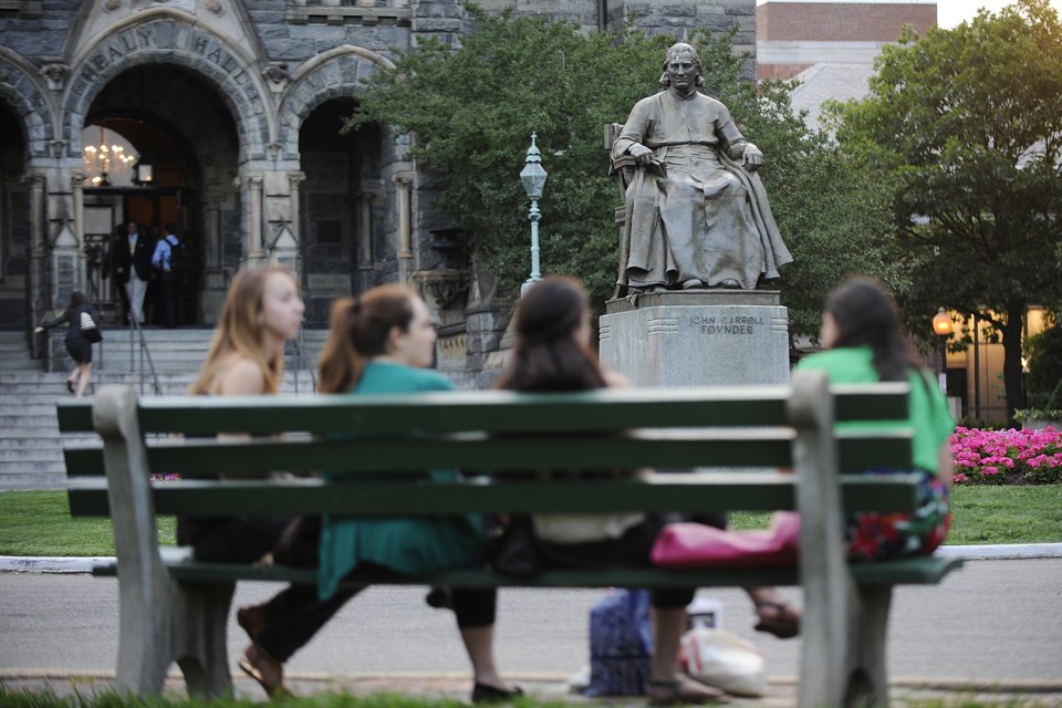 Students sit on a bench in front of a statute of the university founder John Carroll at Georgetown University.
