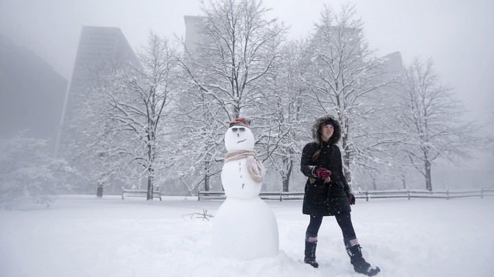 A woman wearing a heavy winter coat walks past a snowman she built in a park during blizzard conditions in Chicago, in 2015.