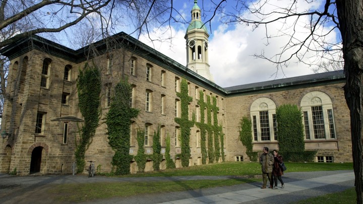 Two people walk past a brick, ivy-covered building on the Princeton University campus.