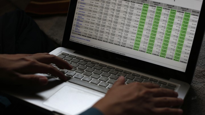 Someone's hands rest on a laptop displaying a large spreadsheet.