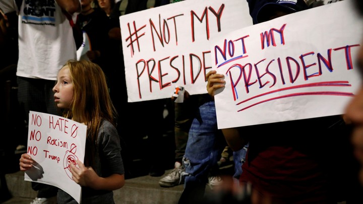 Protesters, including a young girl, hold signs reading "not my president" and "no hate, no racism, no Trump."