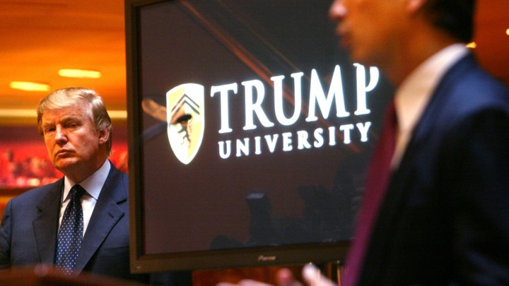 Donald Trump stands next to a screen that reads "Trump University."