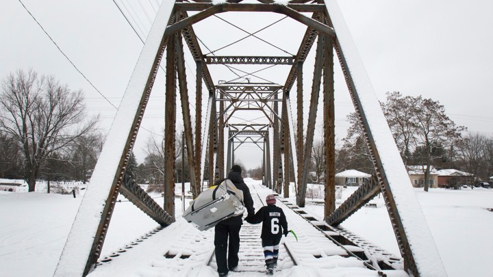 A man and a little boy hold hands while crossing a snowy bridge.
