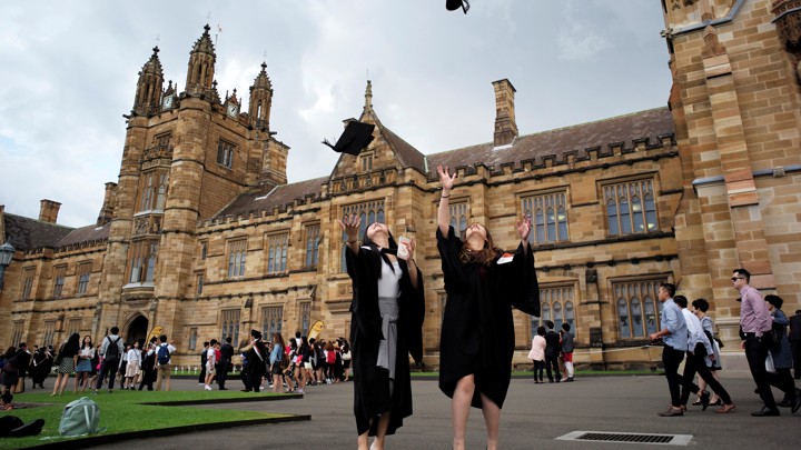Two graduates toss their caps in the air while standing in front of a stately brick building.