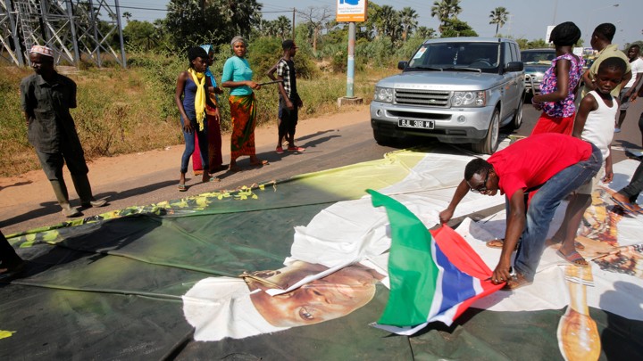 Supporters of President-elect Adama Barrow lay a Gambian flag across a poster of incumbent President Yahya Jammeh.