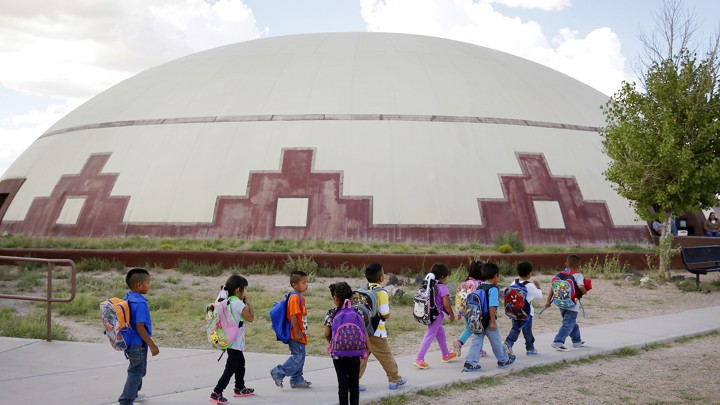 A group of children wearing backpacks walk past a building.