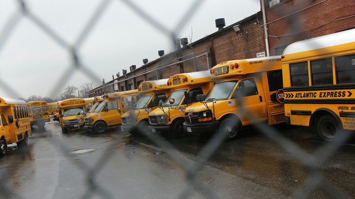 School buses photographed through a chain-link fence.