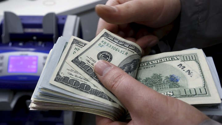 Someone holds a wad of $100 bills.