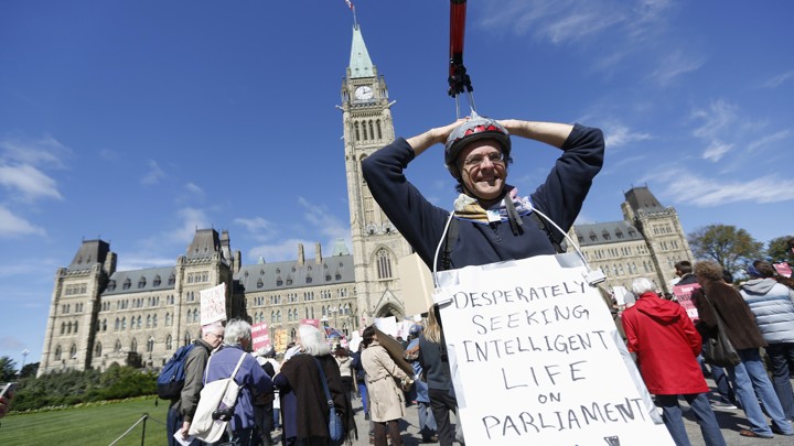 Protester with telescope on head with sign saying, "Desperately seeking intelligent light on Parliament Hill!"