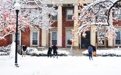 Students have a snowball fight in front of a large brick building with columns.
