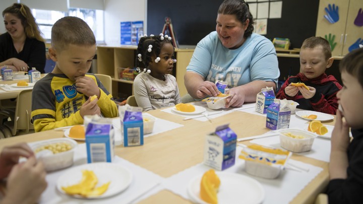 A diverse group of children eats apples and drinks milk.