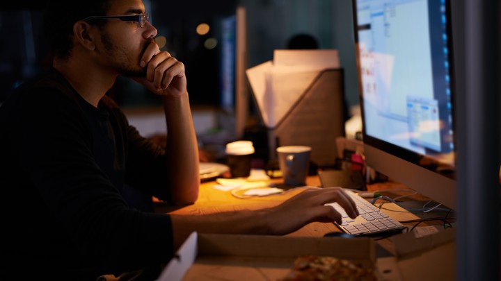 A young man works on a computer in a darkened office.