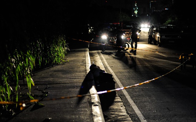 An alleged drug dealer and victim of a summary execution with his head wrapped in tape is examined by police on July 27, 2016, in Manila, Philippines.