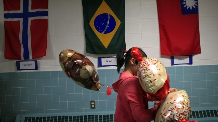 A student carrying balloons walks past the flags of Norway, Brazil, and Taiwan.