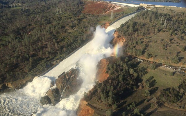 Water pours over the damaged main spillway at the Oroville Dam and over a hillside.