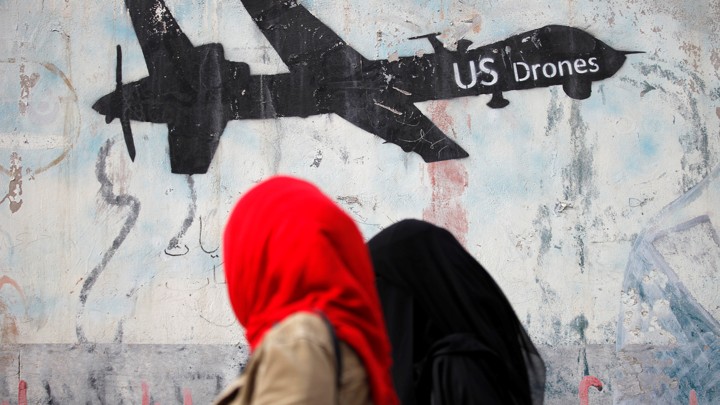 Women walk past a graffiti, denouncing strikes by U.S. drones in Yemen, painted on a wall in Sanaa, Yemen on February 6, 2017.