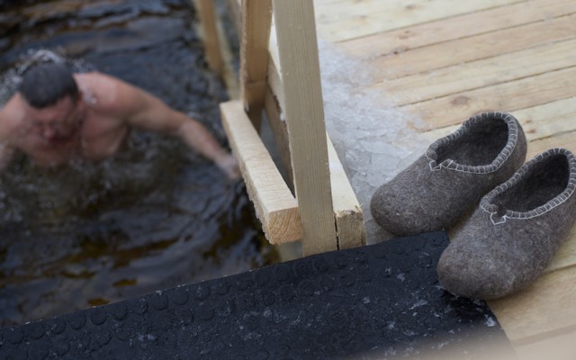 A Russian man eases himself into icy water while his slippers wait on a deck.