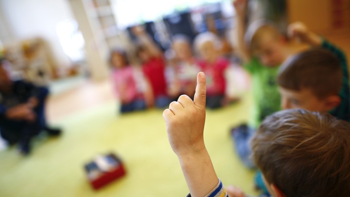 An unrecognizable kindergartener raises his hand