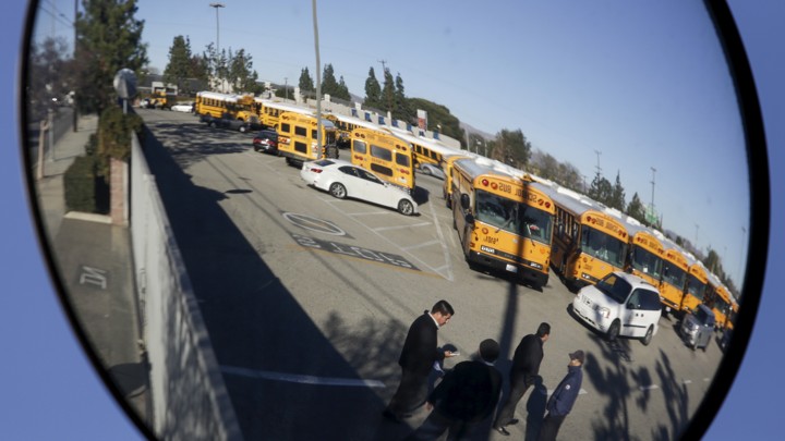 A parking lot filled with school buses is reflected in a bus mirror
