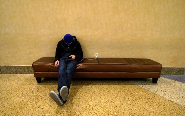 A man sleeps on a couch with his cell phone plugged into a nearby outlet