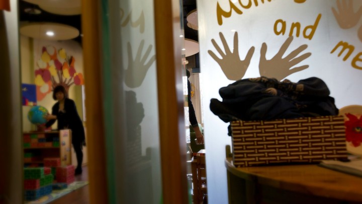 A teacher arranges a globe in a classroom. A sign reads "mommy and me" with handprints around the text.