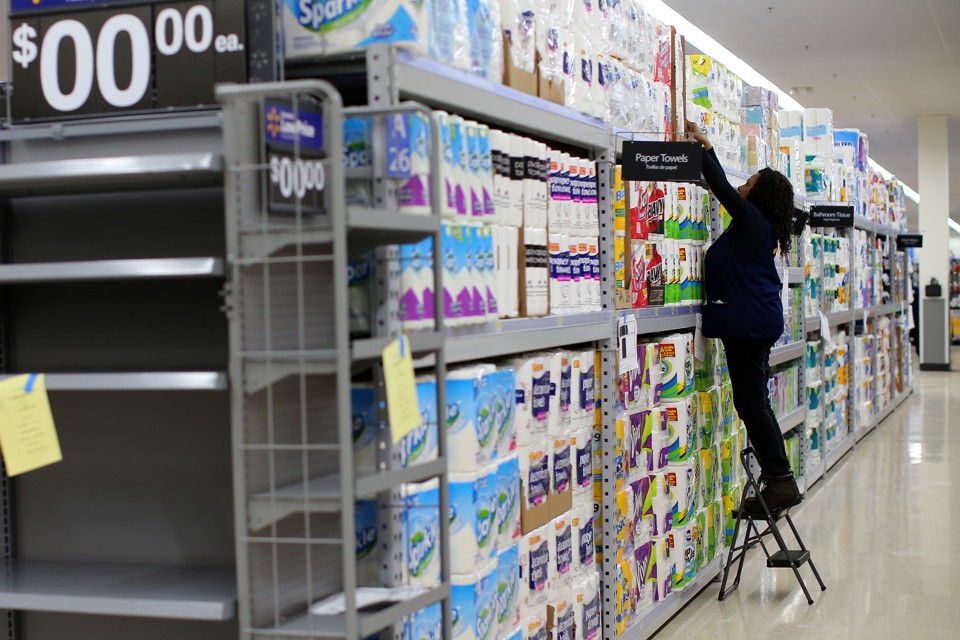 A Walmart employee stocks rolls of paper towels on a shelf.