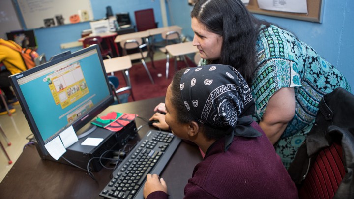 An adult and student huddle around a computer displaying the bright images of comics.