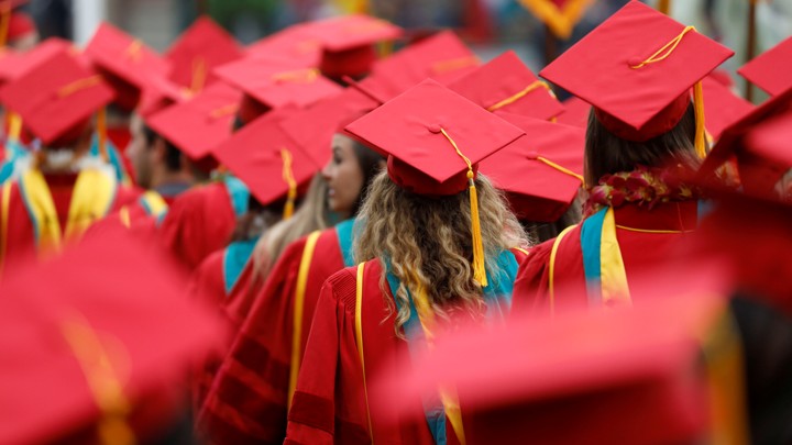 The backs of graduates in red caps and gowns