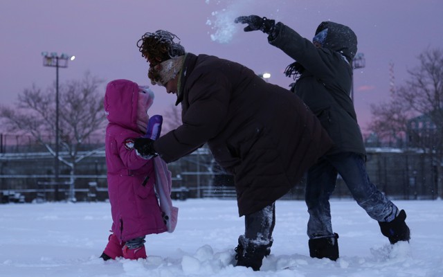 An adult comforts one child while another throws a snowball behind them. 