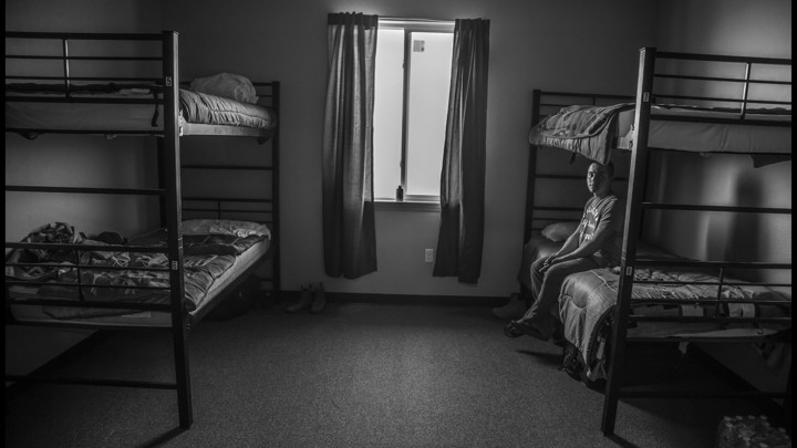 B. Mendoza Vasquez, an H-2A contract worker, sits on a bed in the room he shares with three other farmworkers in a dorm built by his employer.