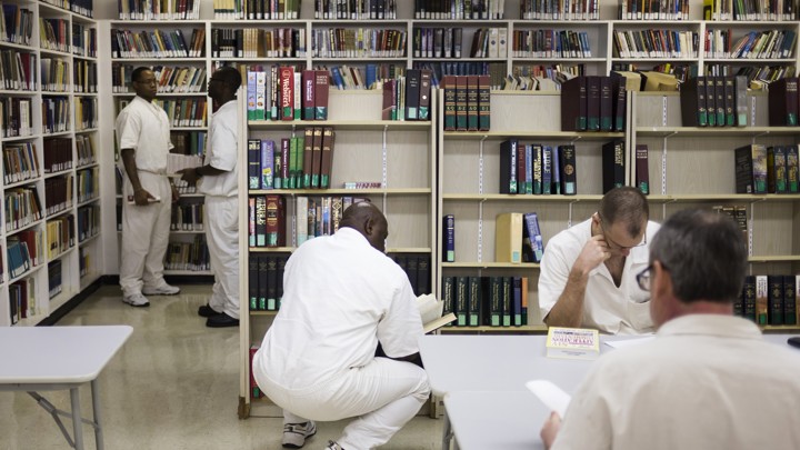 Men dressed in all white sit in a fluorescent room with bookshelves