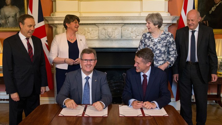 Prime Minister Theresa May stands next to Democratic Unionist Party leader Arlene Foster, as DUP MP Jeffrey Donaldson signs the agreement with Gavin Williamson, Britain's parliamentary secretary to the Treasury and chief whip.