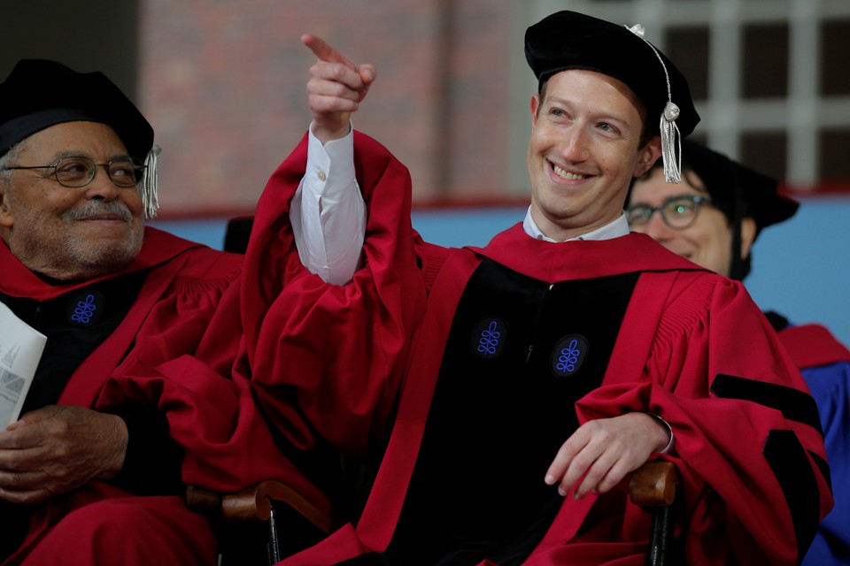 The Facebook founder Mark Zuckerberg points and smiles while wearing a cap at gown at Harvard's commencement