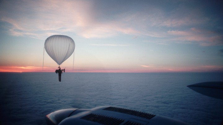 A balloon floats over a body of water with a sunset or sunrise visible in the background.