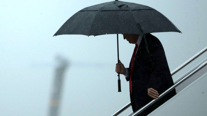 Donald Trump stands underneath an umbrella.