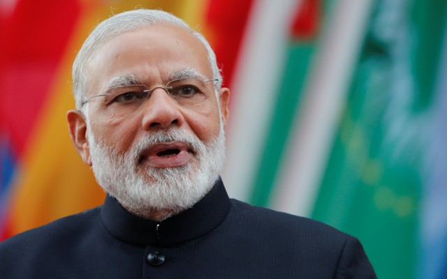 India's Prime Minister Narendra Modi looking at the camera in front of a row of flags.