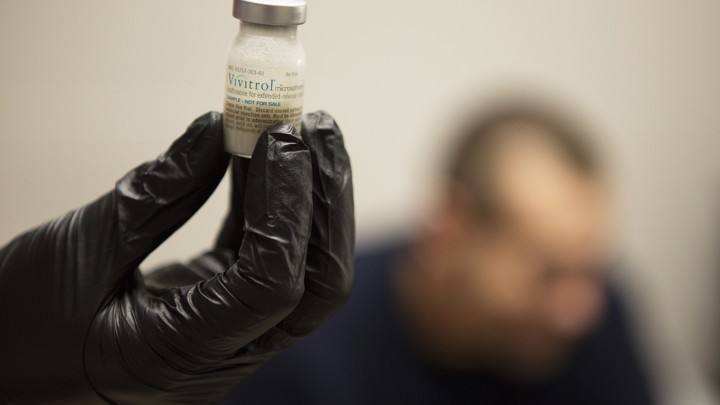 A gloved hand holds a small bottle of white liquid