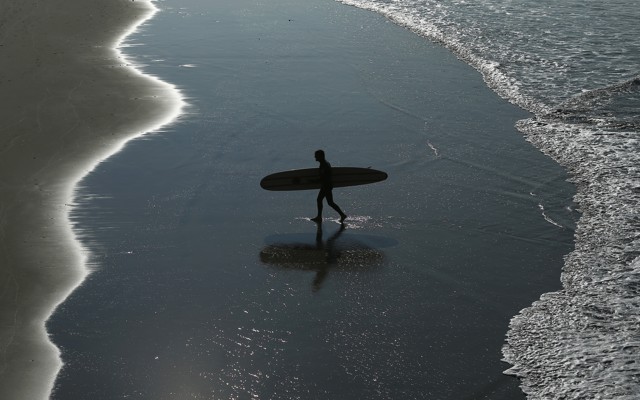A surfer walks on the beach.